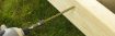 Close-up of a green hex head timber screw being driven into a wooden plank using a power drill, on a grassy outdoor surface