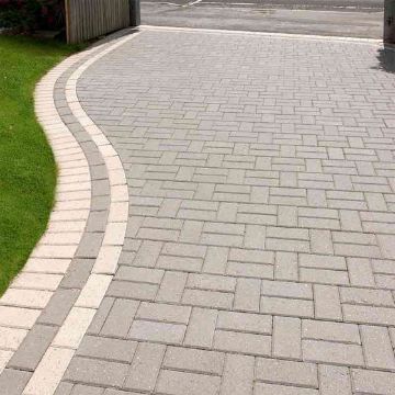 Curved residential driveway featuring Brett Omega 50mm Block Paving in Silver Haze, laid in a herringbone pattern with contrasting light grey edging for a clean, modern finish