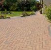 Driveway and garden path paved with Brett Omega 50mm Block Paving in Autumn Gold, laid in a classic herringbone pattern with contrasting grey edging, complementing a well-maintained landscaped garden