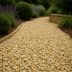Garden path laid with 20mm Cotswold chippings in cream and honey tones, bordered by curved concrete edging and surrounded by lavender, shrubs, and ornamental grasses in soft daylight.