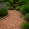 Curved garden path laid with small Forest of Dean pink chippings, bordered by grey concrete edging and surrounded by lavender, ornamental grasses, and a terracotta pot under soft daylight
