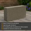Rectangular 100mm dense concrete block placed on a paved patio surface in a landscaped garden, with a brick wall and flowering shrubs in the background. Ideal for structural and loadbearing construction