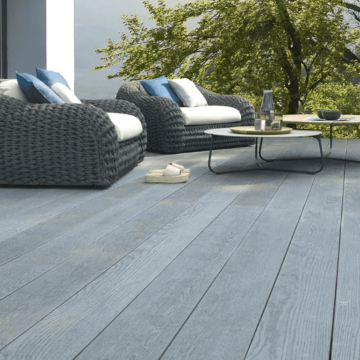 Modern garden patio featuring stylish grey Millboard Enhanced Grain composite decking boards with a realistic wood grain texture, paired with contemporary rattan outdoor furniture and a scenic garden backdrop