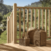 Outdoor timber decking with chamfered and beaded newel posts and vertical spindles, overlooking a lush green garden; a wicker picnic basket and drinks set on the deck evoke a relaxed summer atmosphere